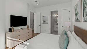 Une chambre moderne avec un grand lit, un téléviseur à écran plat, une commode et un couloir menant à la salle de bain.