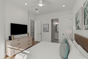 A modern bedroom with a large bed, a flat-screen TV, a dresser, and a hallway leading to a bathroom.