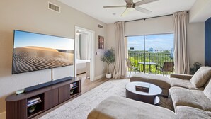 Een moderne woonkamer met een flatscreen televisie, een plafondventilator, een bank, een salontafel en een balkon met buitenmeubilair.