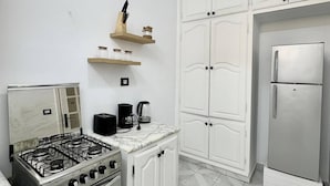 Een keuken met witte kastjes, een gasfornuis, een oven, een koelkast en een koffiezetapparaat.
