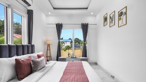A modern bedroom with a large bed, a view of the outdoors, and artwork on the wall.