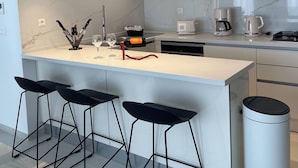 Una cocina moderna con armarios blancos, encimera de mármol, una isla central con taburetes de bar e iluminación colgante.