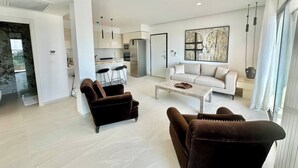 Una sala de estar moderna con un sofá, dos sillones, una mesa de centro y una cocina al fondo.