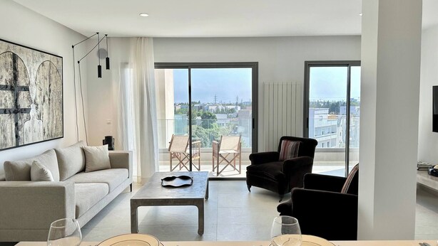 Una sala de estar moderna con un sofá, una mesa de comedor para dos personas y un balcón con sillas.