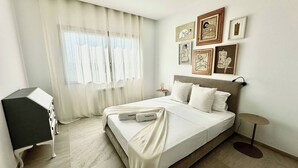 Un dormitorio con cama, escritorio y ventana con cortinas traslúcidas.