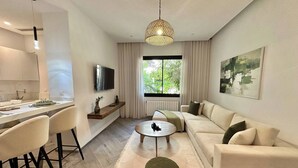 Una sala de estar moderna con un sofá, una mesa de centro, un televisor y una zona de comedor con sillas y una mesa.