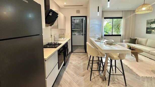 Una cocina moderna con estufa integrada, un refrigerador negro y una zona de comedor con mesa y sillas blancas.
