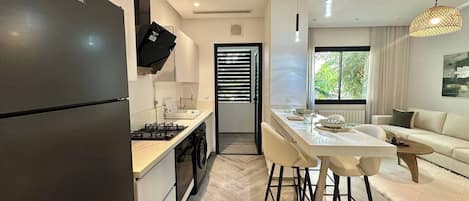 A modern kitchen with a built-in stove, a black refrigerator, and a dining area with a white table and chairs.
