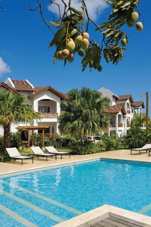 Una piscina con sillas de descanso, un edificio con balcones y palmeras.