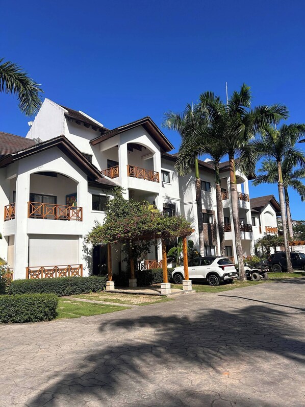 Un hotel de varios pisos con balcones, un espacio de estar al aire libre cubierto y palmeras.
