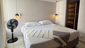 Ein modernes Schlafzimmer mit einem großen Bett, einem Standventilator und zwei Pendelleuchten.