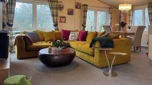 Un salon chaleureux avec un canapé jaune, une table basse ronde et un coin repas agrémenté d’un lustre.