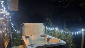 Un bain à remous sur une terrasse en bois, illuminée de guirlandes lumineuses.