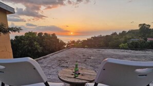 A terrace with two white chairs, a round wooden table, and a bottle of beer.