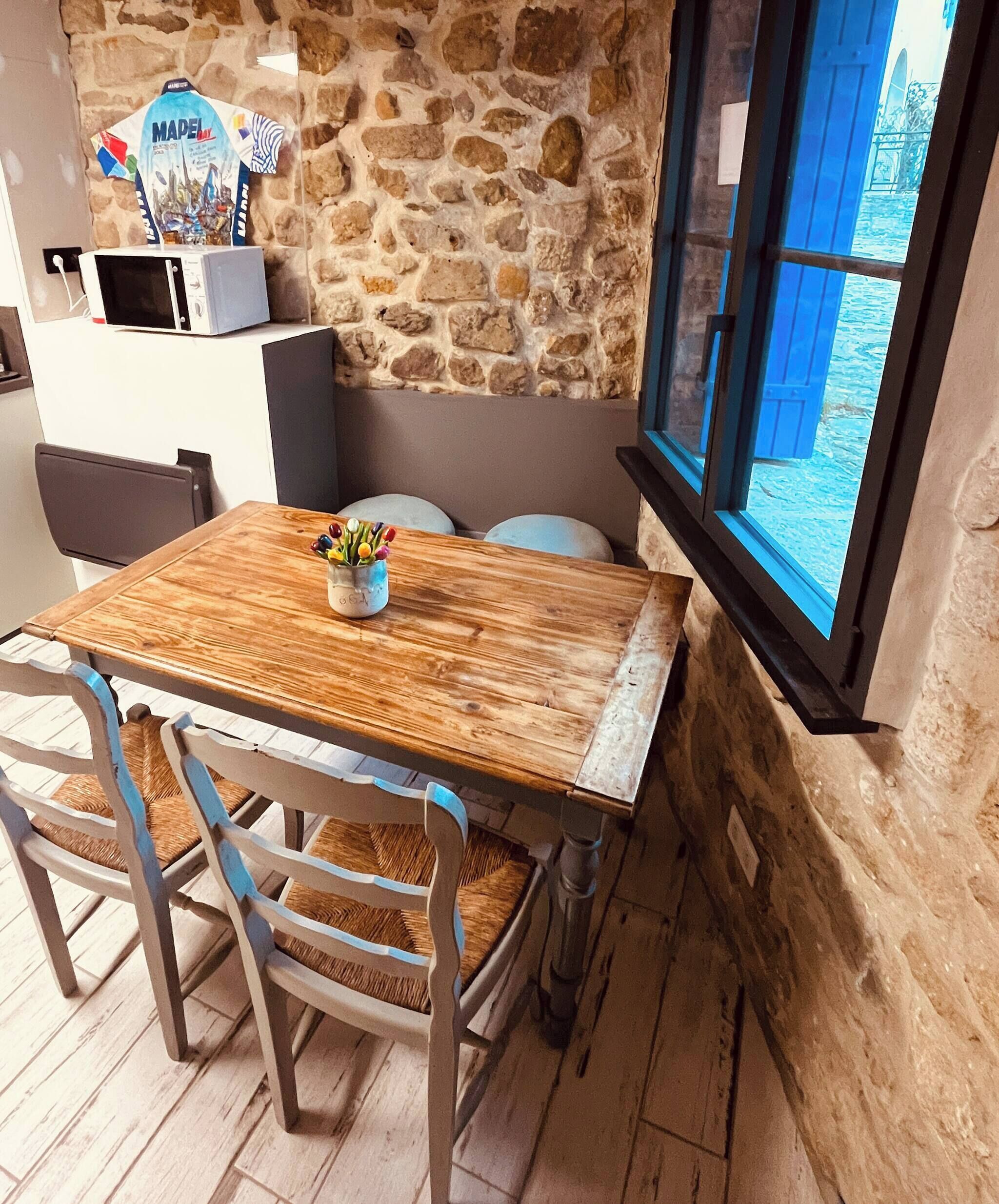 Un mur de pierres apparentes, une table en bois avec des chaises et une fenêtre offrant une belle vue.