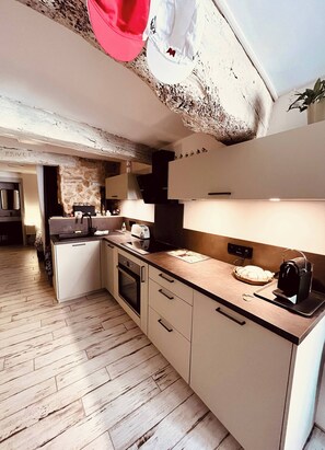 A modern kitchen with a stone accent wall, a built-in oven, and a countertop with a toaster and bread basket. - Musette du Ventoux, Studio for 3 (Bédoin)