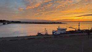Näkymä merenrannalta, jossa auringonlasku, silta ja laituri, jossa on veneitä.