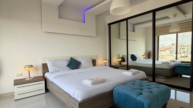 Une chambre à coucher moderne avec un grand lit, des tables de chevet, un miroir et une vue sur la ville.