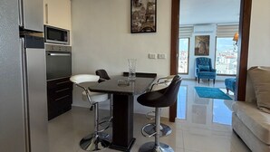 Une cuisine moderne dotée d’appareils électroménagers intégrés, un coin repas avec des tabourets de bar et une vue sur la ville grâce à de grandes fenêtres.