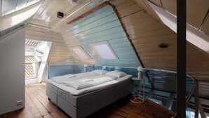 Ett sovrum med ett tak i loftstil, en säng, ett sängbord och ett fönster.