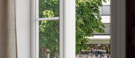 Una habitación con un amplio ventanal que da a una plaza pública con gente y árboles.
