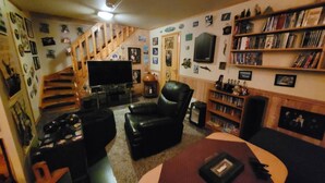 Una sala de estar con televisor, sillón de cuero, estantería y una escalera.