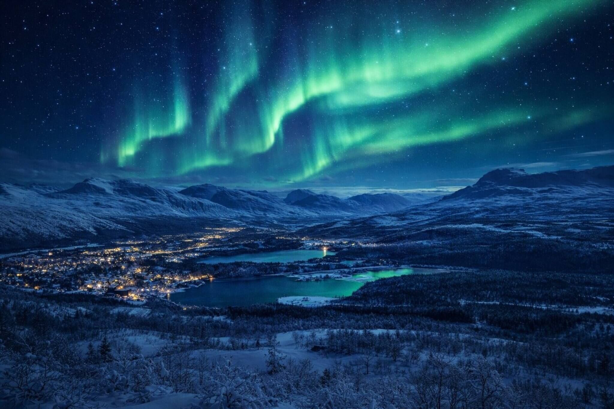 A snowy landscape with a town and a lake, under a night sky with the Northern Lights.