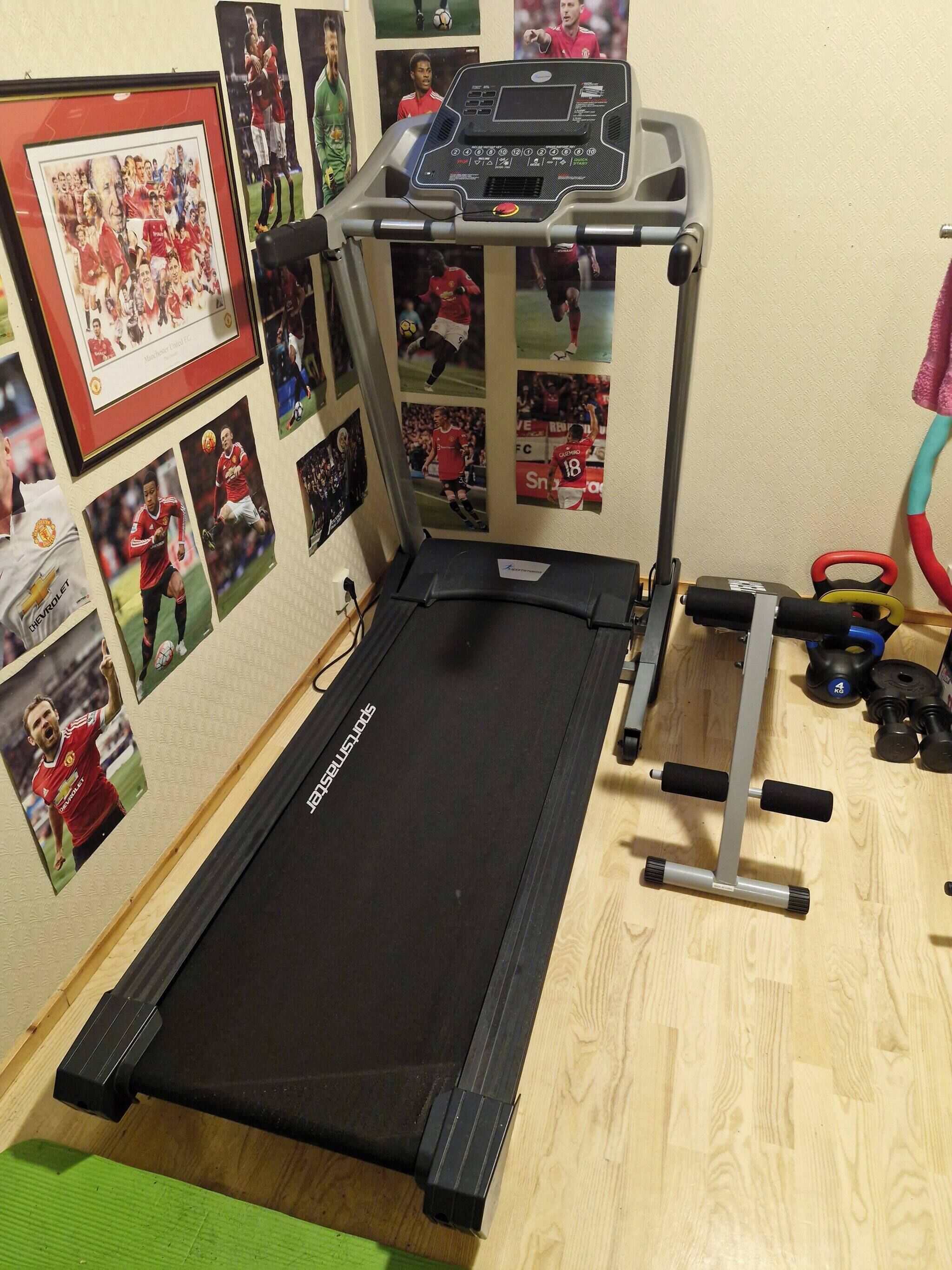 Une salle de sport à domicile équipée d’un tapis de course, d’appareils d’exercice fixés au mur et d’objets de collection liés au sport.