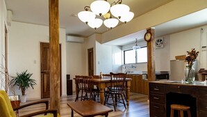 A spacious living area with a wooden dining table, chairs, a sofa, and a kitchen in the background.