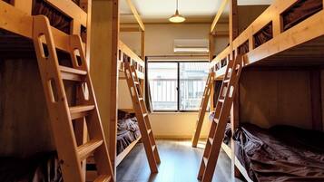 A dormitory room with bunk beds, a ladder, a window, and an air conditioning unit.