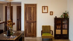 A room with a wooden door, a green armchair, a cabinet with glass doors, and a vase with dried flowers on a table.