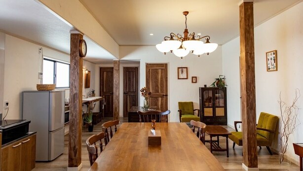 A spacious dining area with a long wooden table, surrounded by chairs, a chandelier, and wooden accents.