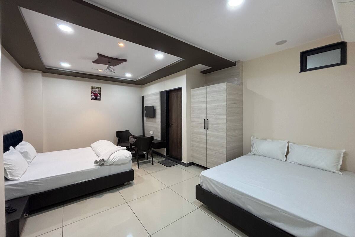 A hotel room with two beds, a desk, a chair, a wardrobe, and a ceiling fan.