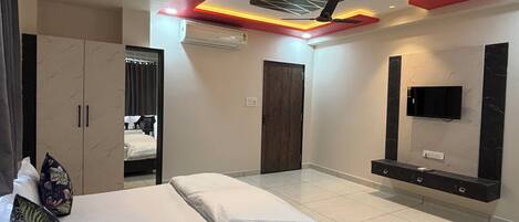 A modern bedroom with a bed, wardrobe, air conditioning unit, ceiling fan, and a mounted TV.