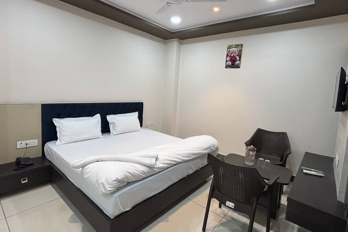 A hotel room with a bed, bedside table, chair, desk, and a television.