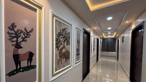 A hallway with framed artwork, a marble floor, and doors on both sides. - Hotel Shri Ram Legacy (Jodhpur)