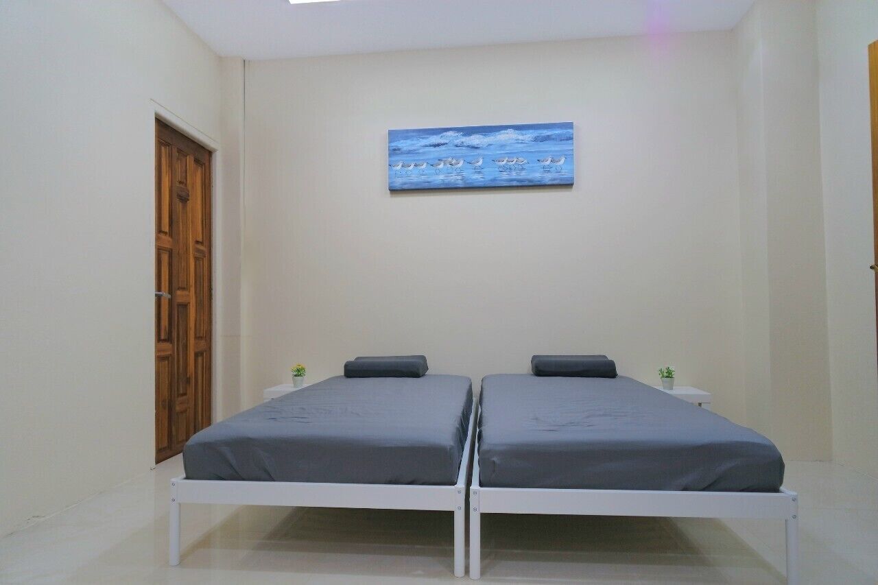 Ein Zimmer mit zwei Einzelbetten, einer Holztür, einer kleinen Pflanze und einem Bild an der Wand.