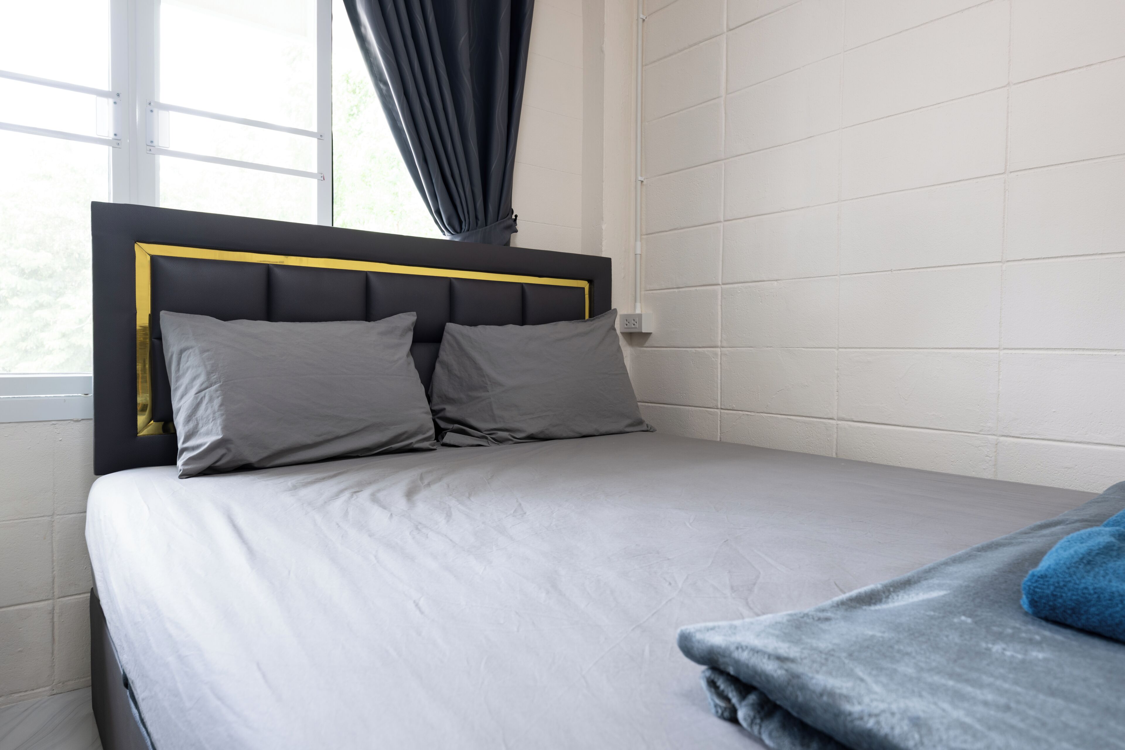 A bed with a black headboard and two pillows, a grey blanket, and a window with curtains.