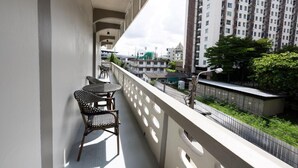 Un balcón con dos sillas y una mesa, con vistas a un paisaje urbano con edificios altos y áreas verdes.