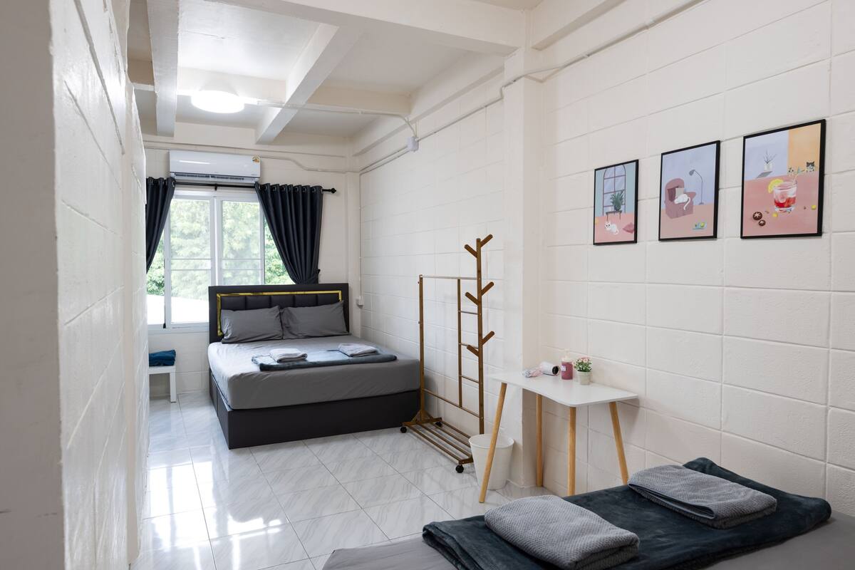 A modern hotel room with a bed, bedside table, and a small window with curtains.