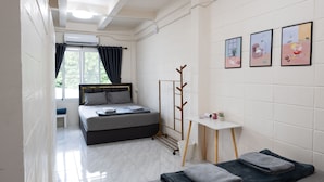 Una habitación de hotel moderna con cama, mesita de noche y un pequeño ventanal con cortinas.