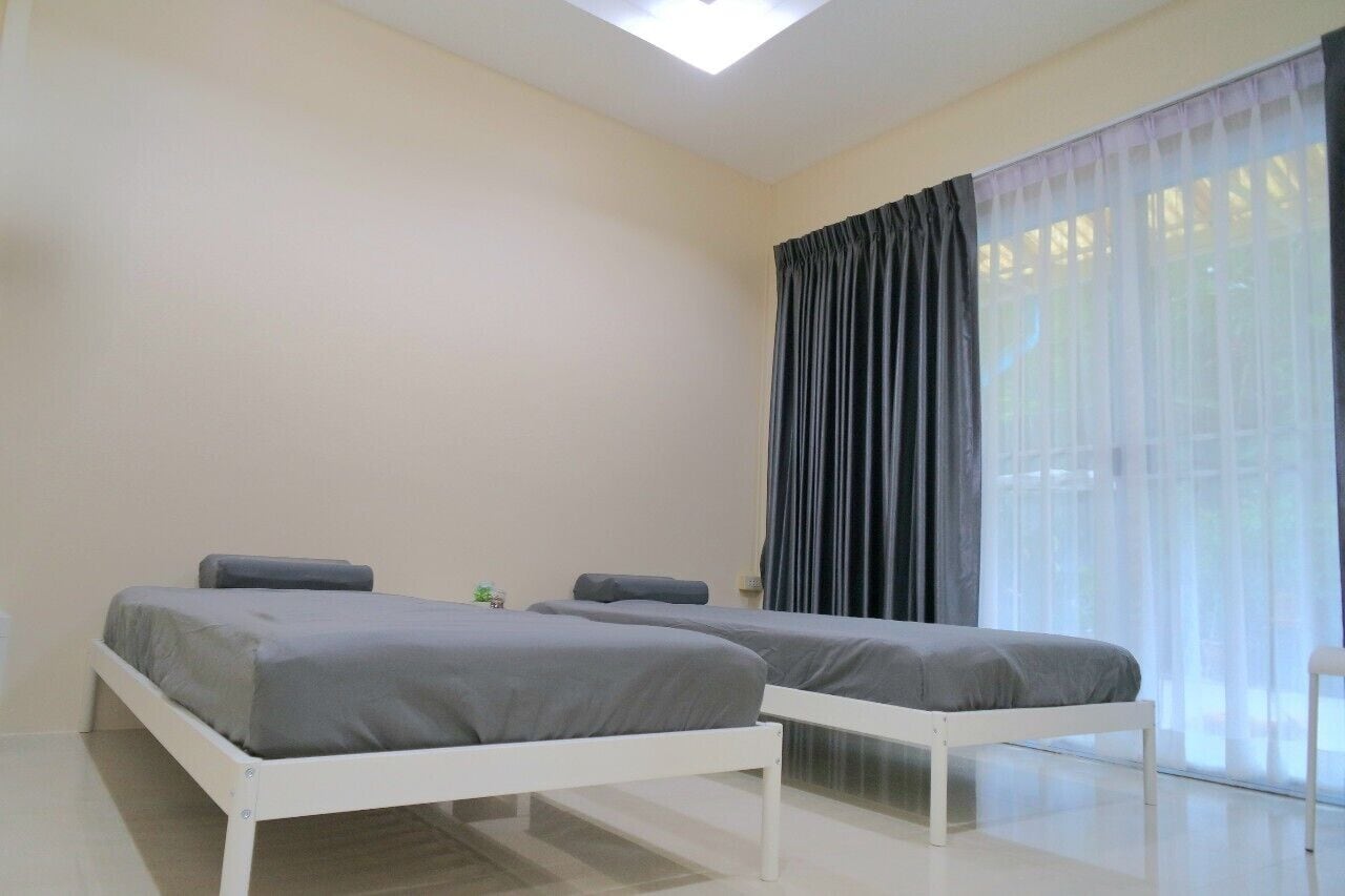 Una habitación con dos camas, un ventanal con cortinas translúcidas y un tragaluz.