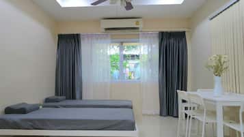 A bedroom with two beds, a ceiling fan, an air conditioning unit, a window with curtains, and a small table with chairs.