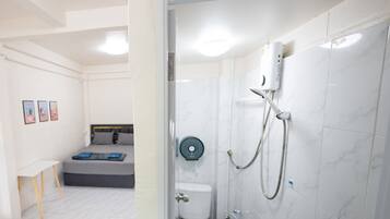 Un baño moderno con ducha, inodoro y una cama en la habitación contigua.