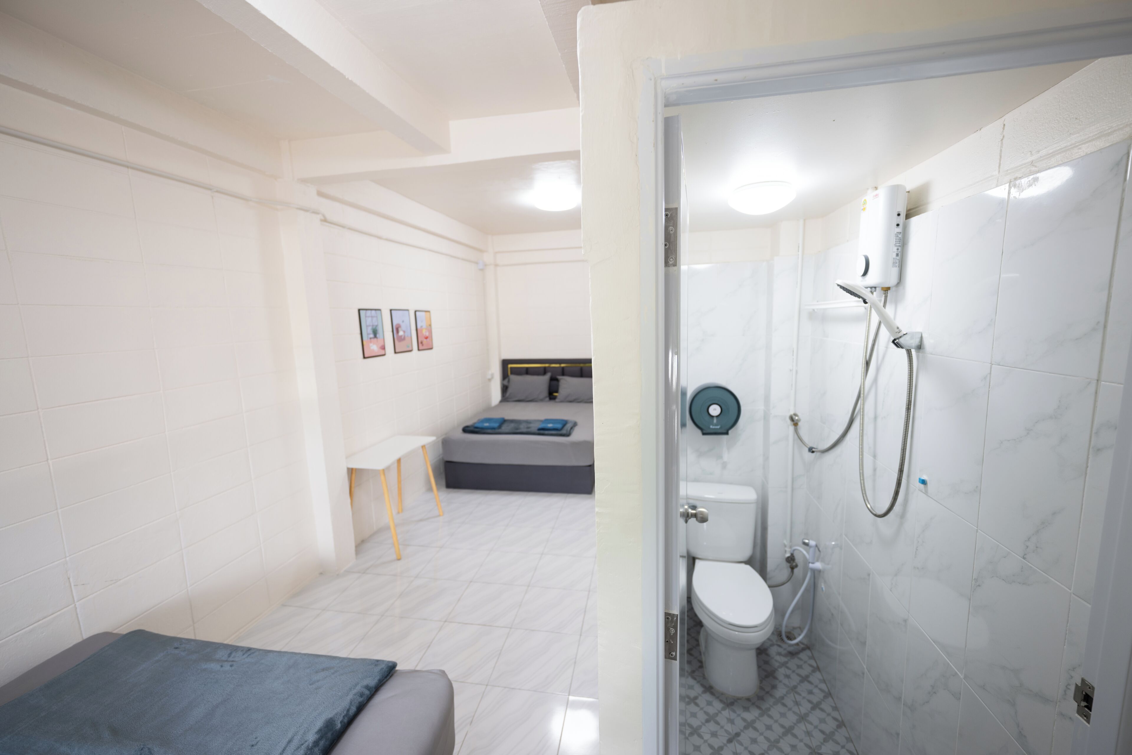 A modern bathroom with a shower, toilet, and a bed in the adjacent room.