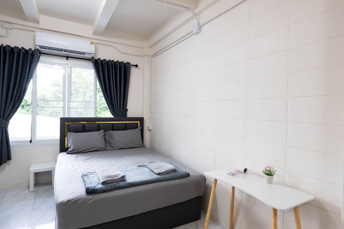 A bedroom with a bed, a bedside table, a window with curtains, and a small potted plant.