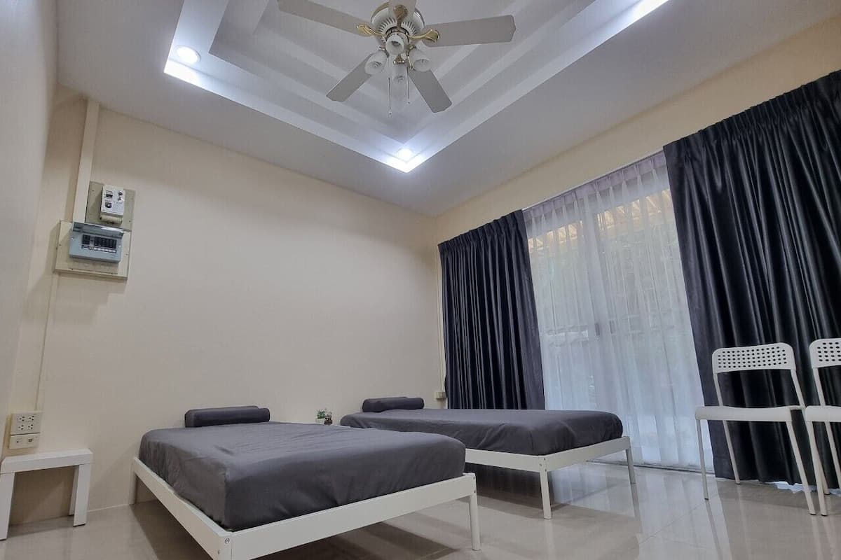A hotel room with two beds, a ceiling fan, a window with curtains, and a small table.