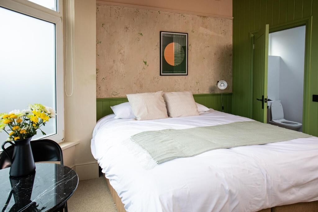 A bedroom with a bed, a vase with flowers, a table, and a green door.