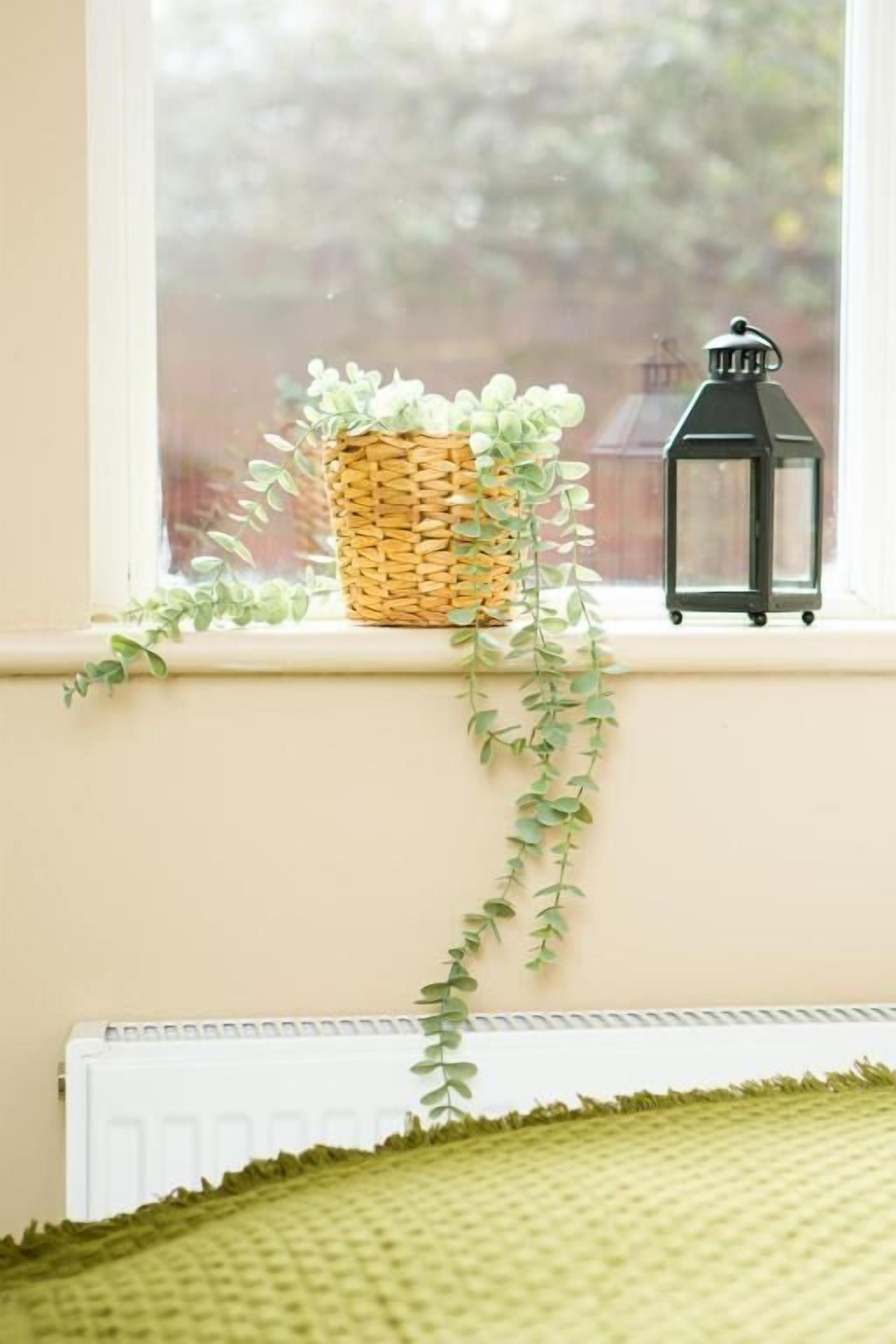Un rebord de fenêtre orné d’un panier en osier, d’une plante suspendue et d’une lanterne.