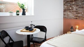 A hotel room with a bed, a small table with a tray of items, two chairs, a radiator, a brick wall, and a window with plants. - Settle Southampton (Southampton)
